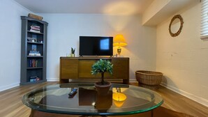 A living room with a glass coffee table, a television on a stand, a bookshelf, a potted plant, and a wicker basket. - City Vibes + Nature Trails! Relax in our comfy 2BR—perfect base for exploring Johnson City & beyond. (Johnson)
