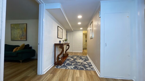 A hallway with wooden flooring, a dark blue patterned rug, a white door, and a green couch with cushions. - City Vibes + Nature Trails! Relax in our comfy 2BR—perfect base for exploring Johnson City & beyond. (Johnson)