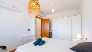 Een slaapkamer met een bed, een kledingkast, een hanglamp en een plant.