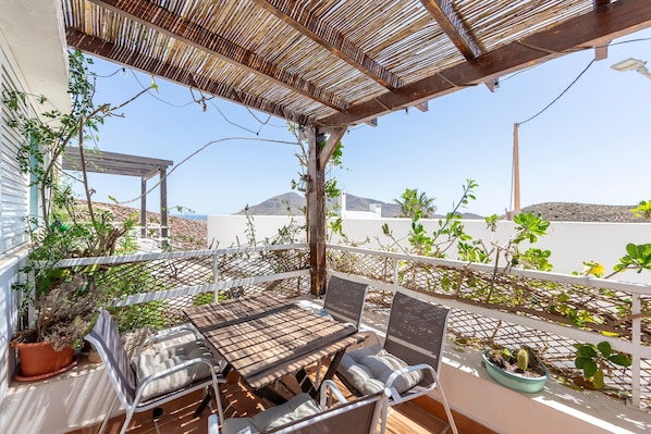 A covered outdoor seating area with a table and chairs, surrounded by potted plants and a view of the landscape.