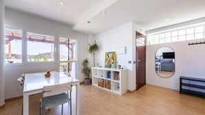 Een ruime woonkamer met een eettafel, boekenkasten, een kamerplant en een groot raam met uitzicht.