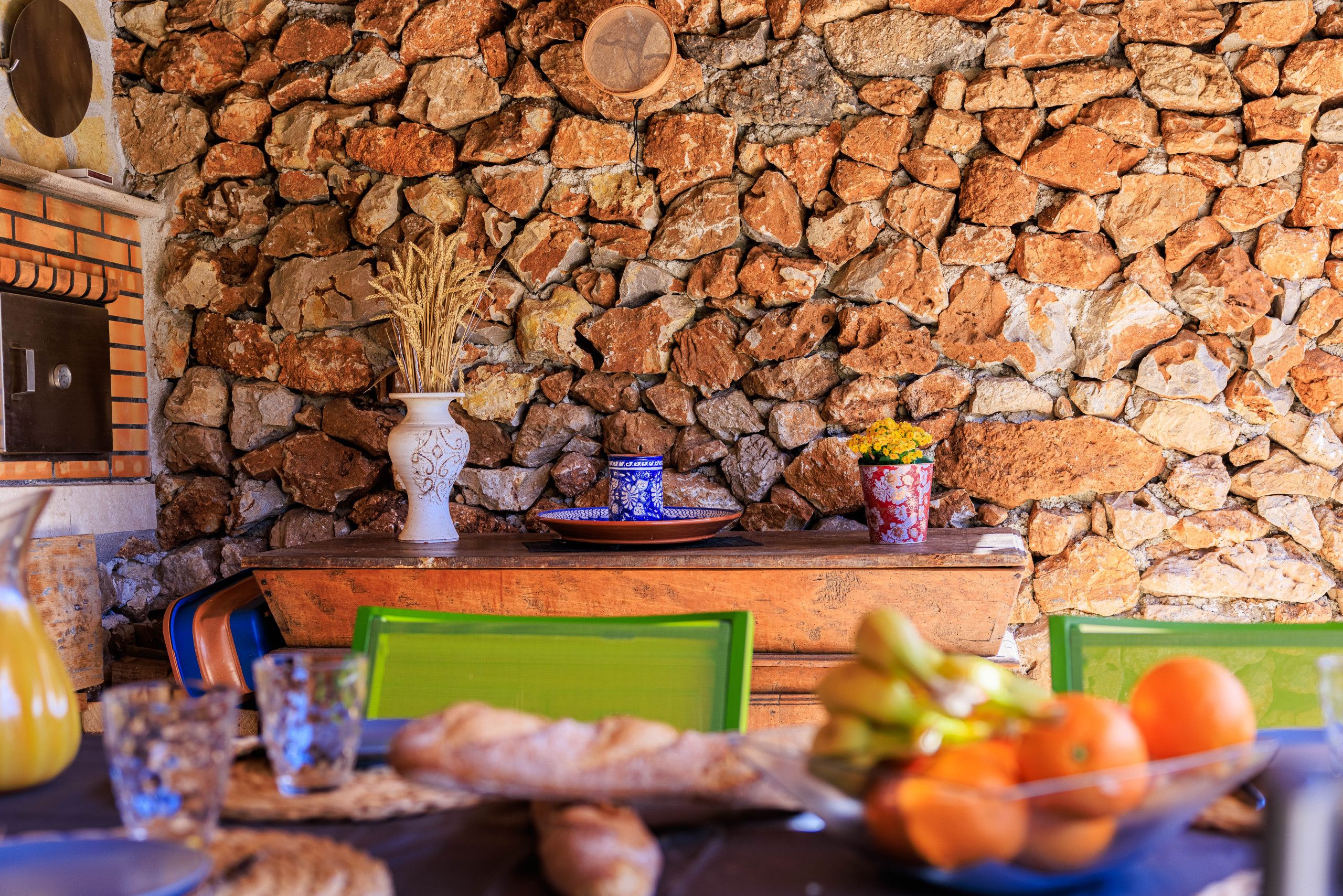 A rustic dining area with a stone wall, wooden table, and chairs.