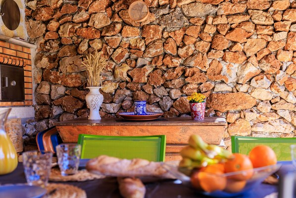 A rustic dining area with a stone wall, wooden table, and chairs.