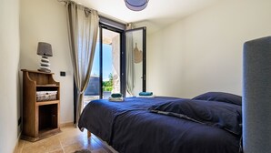 A bedroom with a bed, a nightstand, a lamp, and a view of the outdoors. - Le petit Mas - Calme 5mn from Vence (Vence)