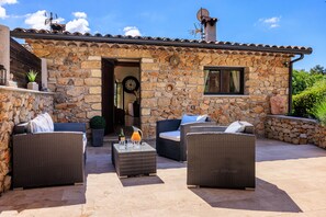 An outdoor patio area with wicker furniture, a stone wall, and a door leading to the interior.