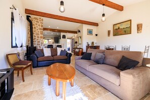 A cozy living room with a stone wall, wooden beams, a fireplace, and a large sofa.