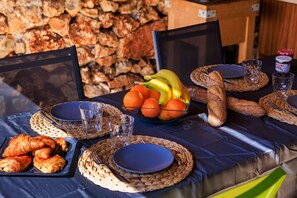 A table set with bread, fruits, and pastries, with a stone wall in the background.