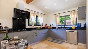 A modern kitchen with grey cabinets, a black countertop, and a dishwasher. There are two windows with curtains, a sink, and a coffee machine. - Le petit Mas - Calme 5mn from Vence (Vence)