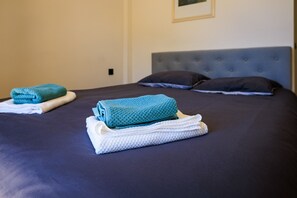 A neatly made bed with a dark blue bedspread, two pillows, and folded towels in blue and white.