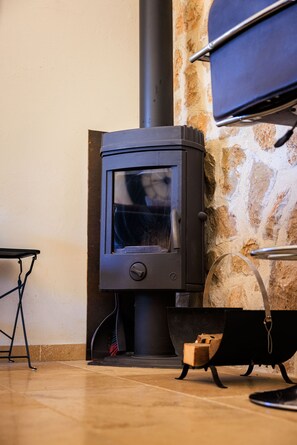 A wood stove in a room with a stone wall and a metal table.