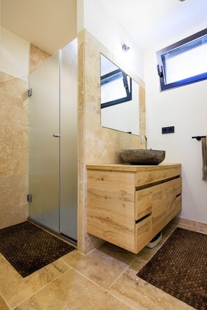 A bathroom with a wooden vanity, a stone sink, a glass shower enclosure, and a large mirror.