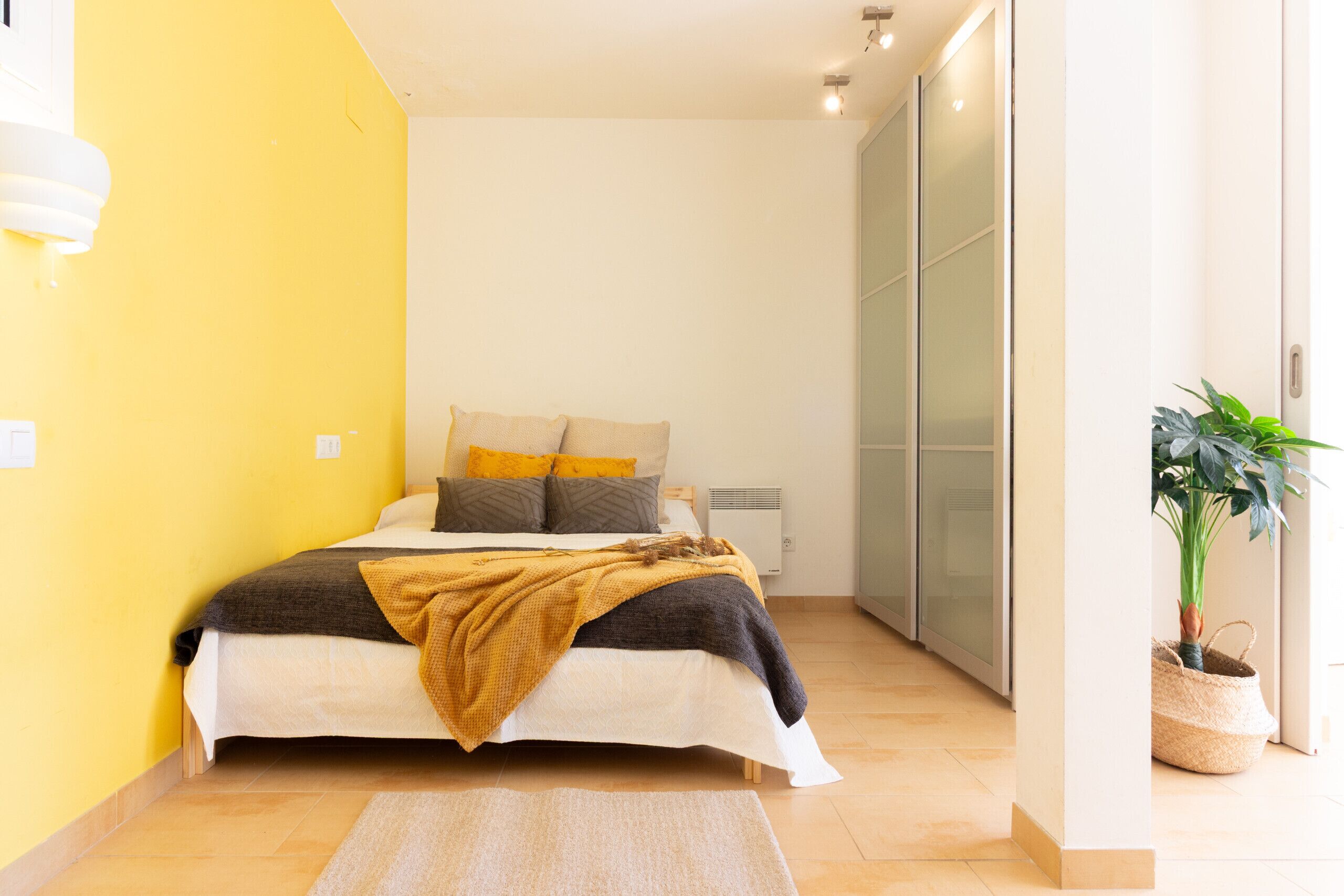 Ein Schlafzimmer mit einem Bett, einem Nachttisch, einer Wandheizung, einer Topfpflanze und einem Schiebetürenschrank.
