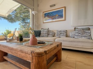 A living room with a wooden coffee table, a sofa, a painting, and a view through a window.