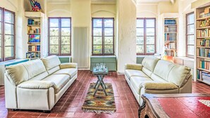 Un salon spacieux avec deux canapés beige, une table basse et une table rouge. De grandes fenêtres laissent entrer la lumière naturelle et offrent une vue sur la verdure environnante.