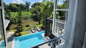 Une vue depuis un balcon donnant sur une piscine, le tout entouré d’une végétation luxuriante et d’arbres.