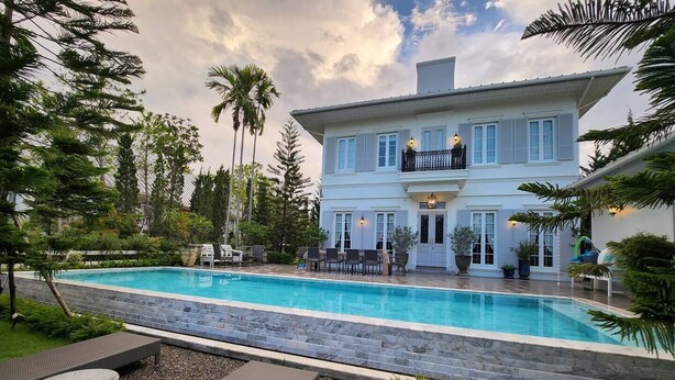 Une grande maison à deux étages dotée d’une piscine, de mobilier d’extérieur et d’un jardin bien entretenu.