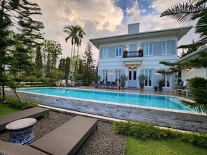 Ein großes, zweistöckiges Haus mit Swimmingpool, Gartenmöbeln und einem gepflegten Garten.