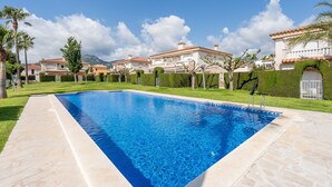Una piscina con un deck de piedra, rodeada de setos cuidados y palmeras.