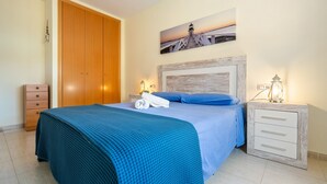 Un dormitorio con una cama, un armario de madera, una mesita de noche con una lámpara y un cuadro en la pared.