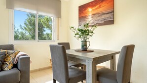 Un comedor con una mesa de madera, sillas tapizadas en gris, un florero con flores y un cuadro de atardecer en la pared.