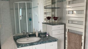 A modern bathroom with a double sink vanity, a glass shower enclosure, a white tiled floor, and a white towel rack. - ROOM RENTAL for events on the Sarthe racetrack (Change)