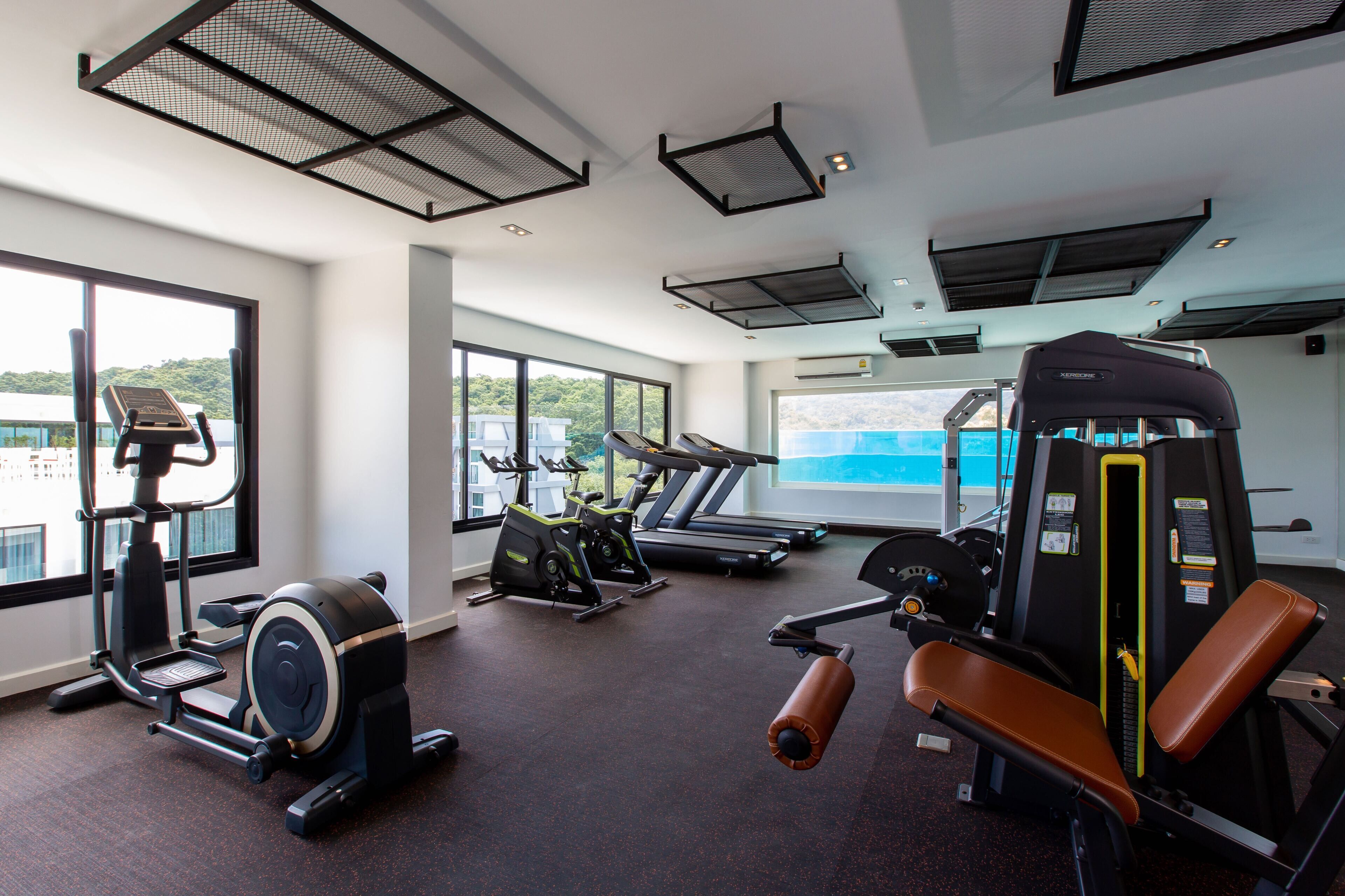 A gym with cardio machines, weight training equipment, and large windows offering views of the outdoors.