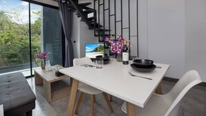 Un espace repas moderne avec une table blanche, des chaises et un bol noir. On peut voir un vase avec des fleurs et une bouteille sur la table.