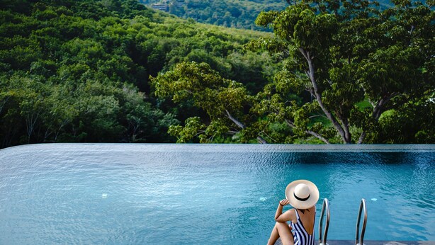 Une personne assise au bord d’une piscine, avec en arrière-plan une végétation luxuriante.