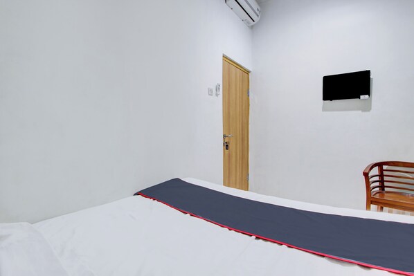 Una habitación con una cama, una puerta de madera, un televisor montado y una silla.