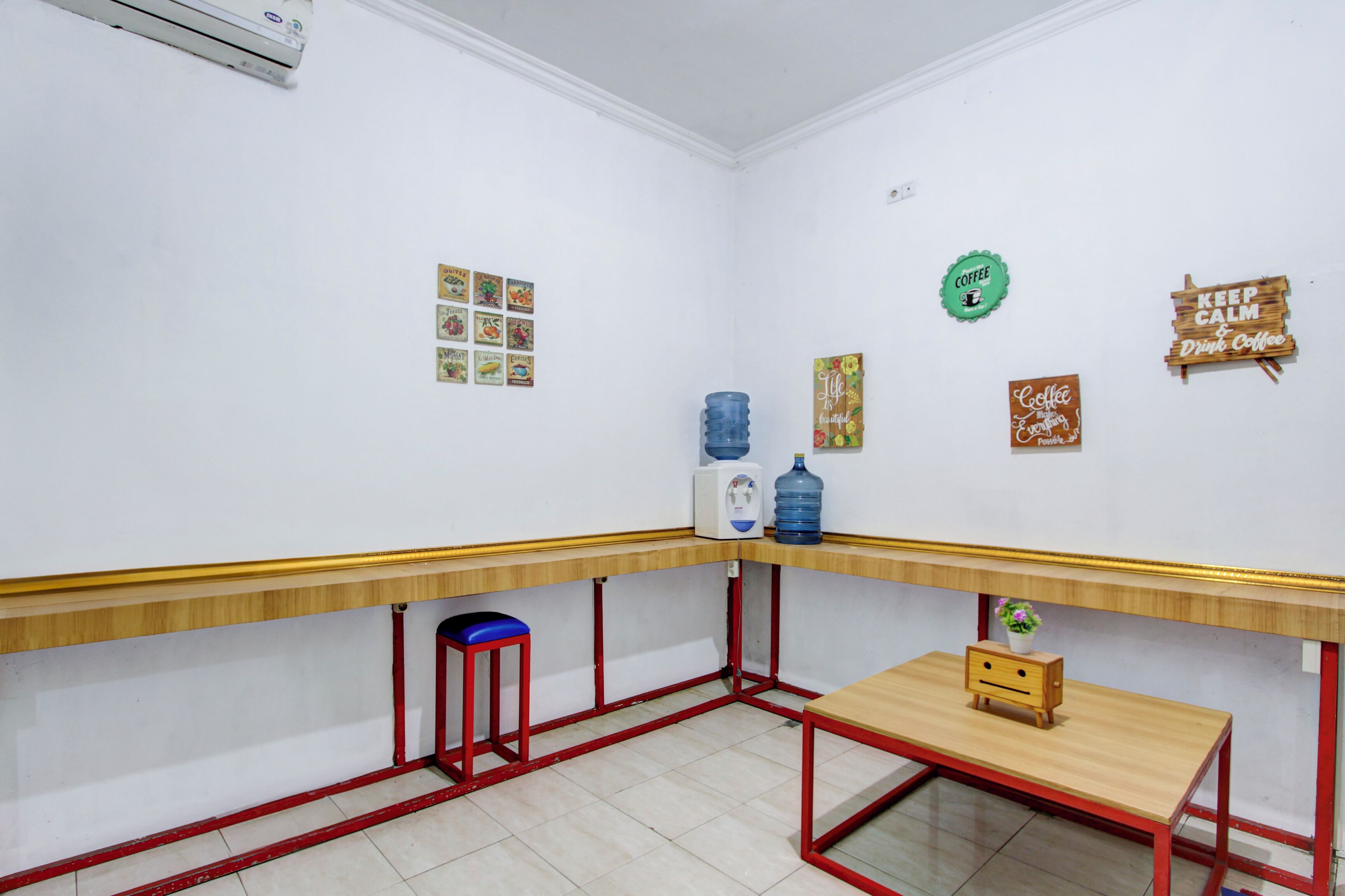 A small, clean room with a wooden table, a red stool, and a water dispenser.