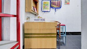 A reception desk labeled "FRONT DESK" with a wooden counter, a chair with a red cushion, and a wall with framed posters. - Hotel O Yogyakarta near Gembiraloka Zoo formerly Paddington Bear Homestay (Banguntapan)