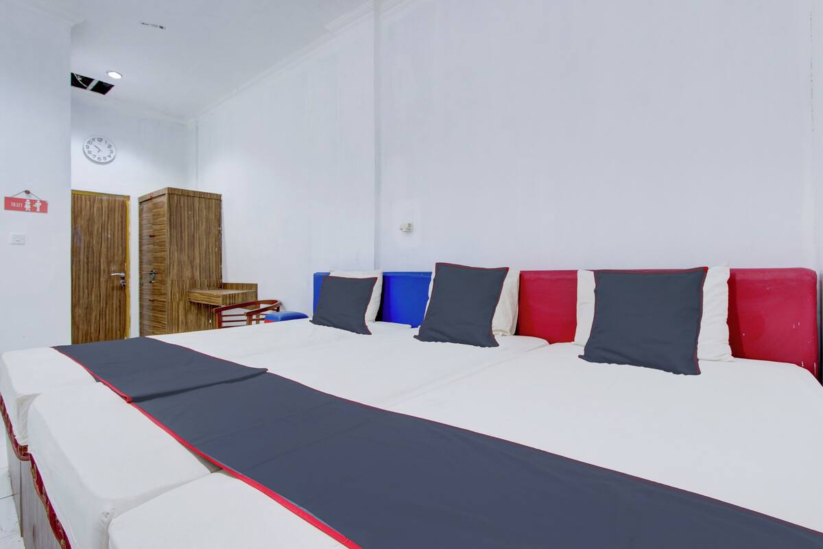 A hotel room with a large bed, a wooden wardrobe, a small table, and a clock on the wall.