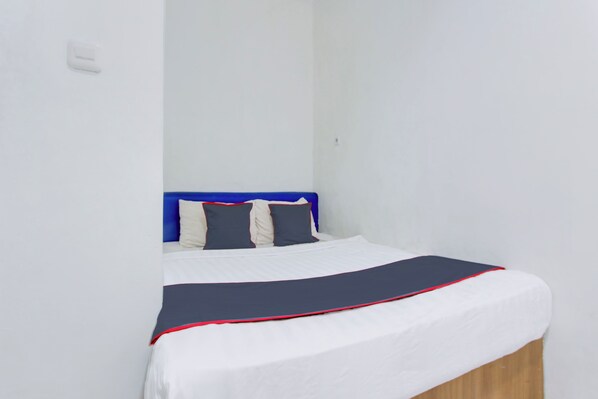 Una cama individual con colchón blanco, cabecera azul y colcha azul marino con detalle rojo.