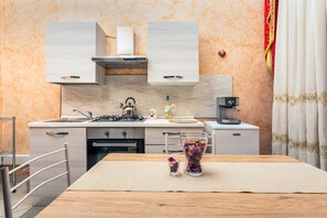 A modern kitchen with a gas stove, sink, and white cabinets. There is a dining table with a vase and a glass.