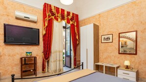 Ein Hotelzimmer mit Bett, Fernseher, Schreibtisch, Lampe, einem Bilderrahmen und einem Fenster mit Vorhängen.