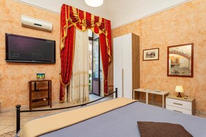 A hotel room with a bed, a TV, a desk, a lamp, a picture frame, and a window with curtains.