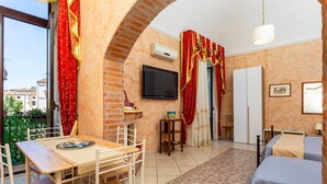 Ein Zimmer mit Backsteinwand, Fernseher, Tisch mit Stühlen, Bett und einem Fenster mit Vorhängen.