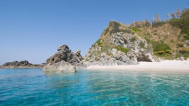 Uma praia com águas turquesa cristalinas, formações rochosas e areia branca.