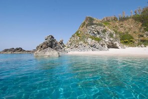Una playa con agua turquesa cristalina, formaciones rocosas y arena blanca.