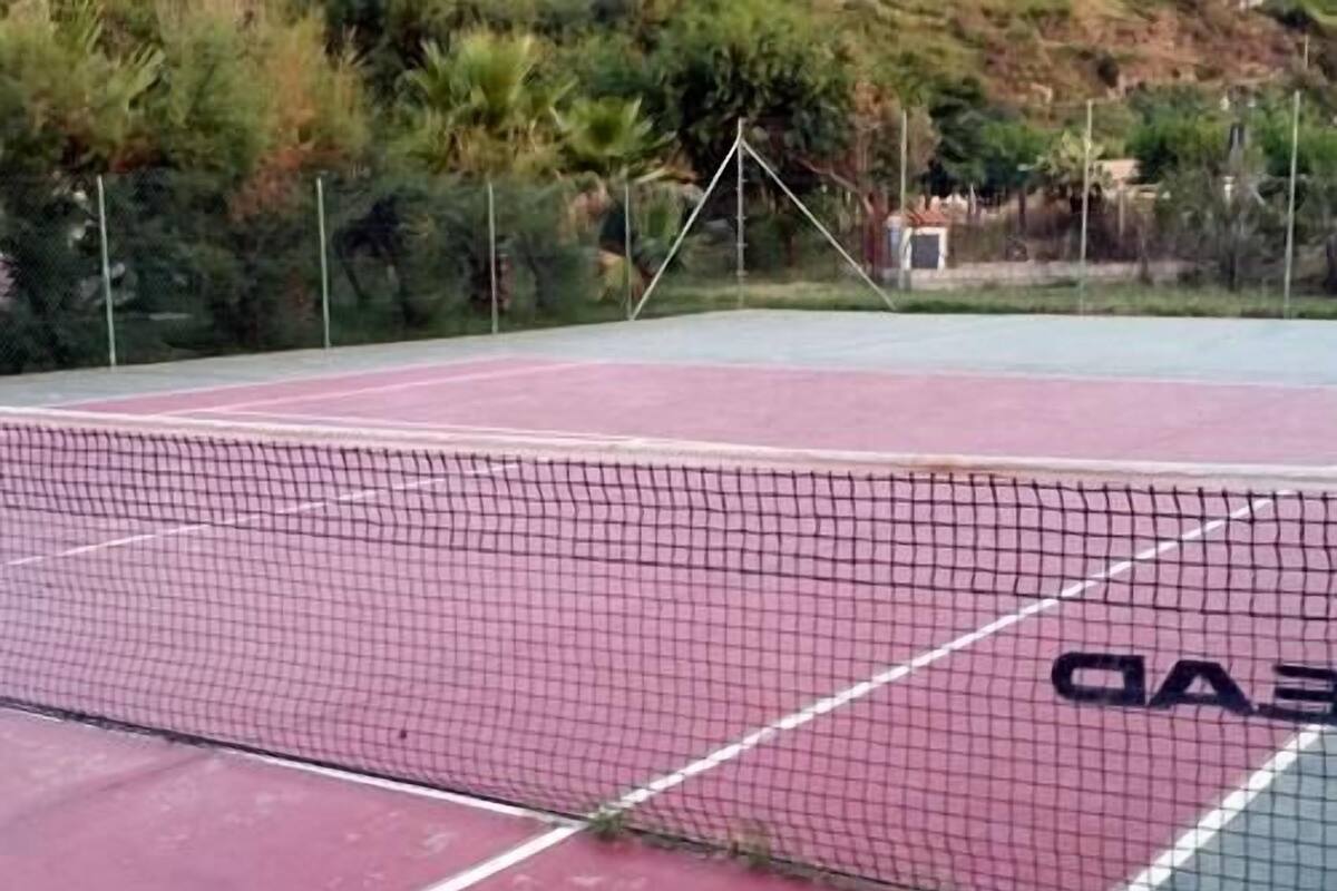 A tennis court with a net, surrounded by a fence and trees.