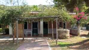 Uma área de estar coberta ao ar livre, com um caminho de tijolos que leva a um edifício com porta verde e janelas.