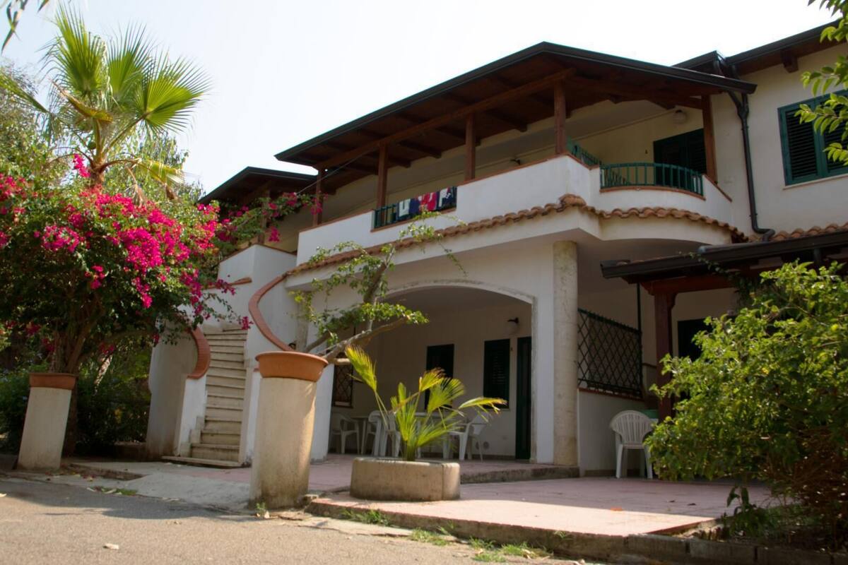 A two-story building with a balcony, potted plants, and outdoor seating.
