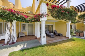 Un bâtiment jaune orné de colonnes blanches, un patio couvert avec des fauteuils et un espace jardin.