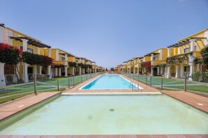Une piscine à l’eau d’un bleu cristallin, entourée de bâtiments jaunes aux colonnes blanches et agrémentée de fleurs rouges.