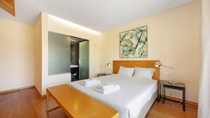 Een hotelkamer met een bed, nachtkastje, lamp en een schilderij aan de muur.