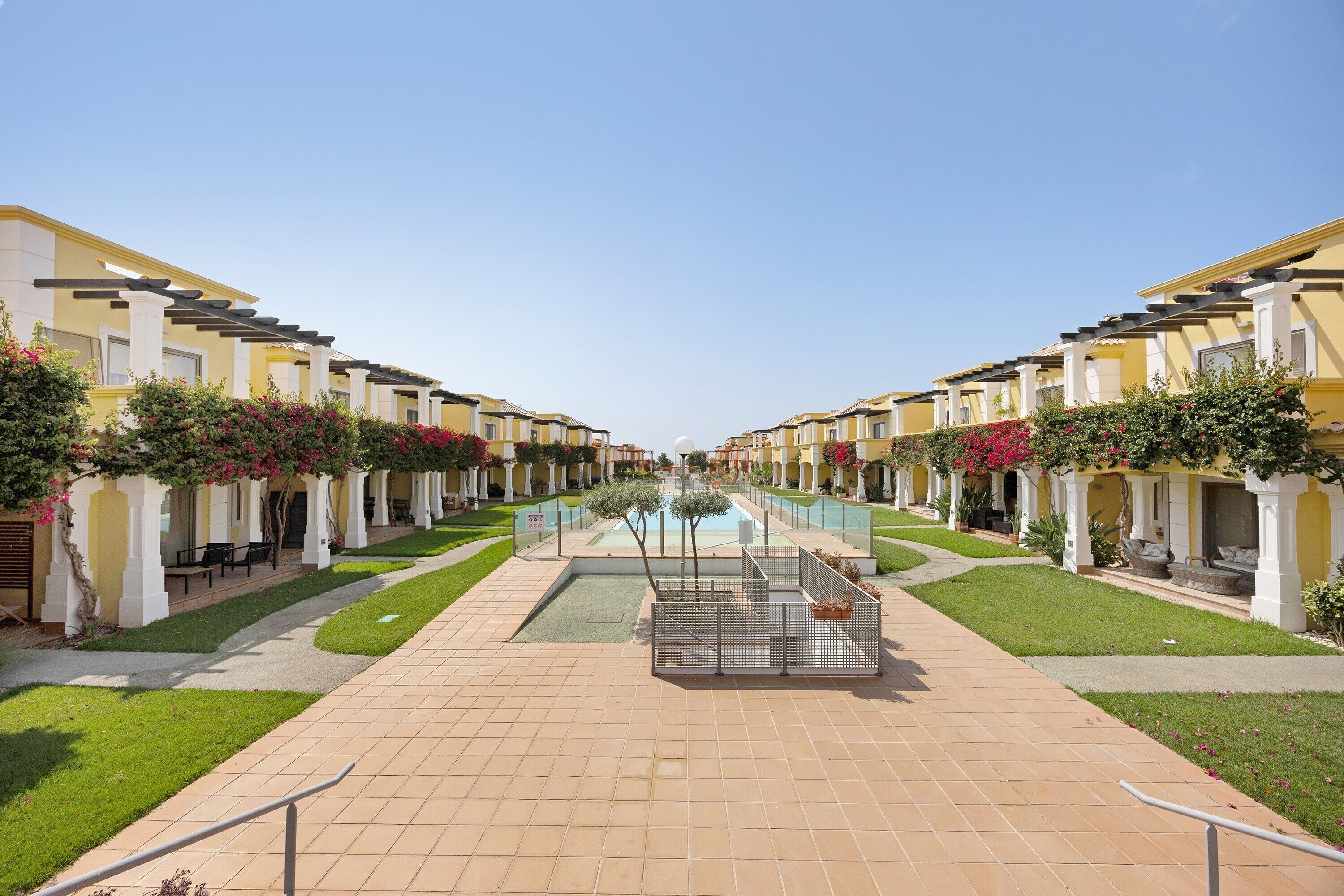 A hotel corridor with a central pool, outdoor seating, and greenery.