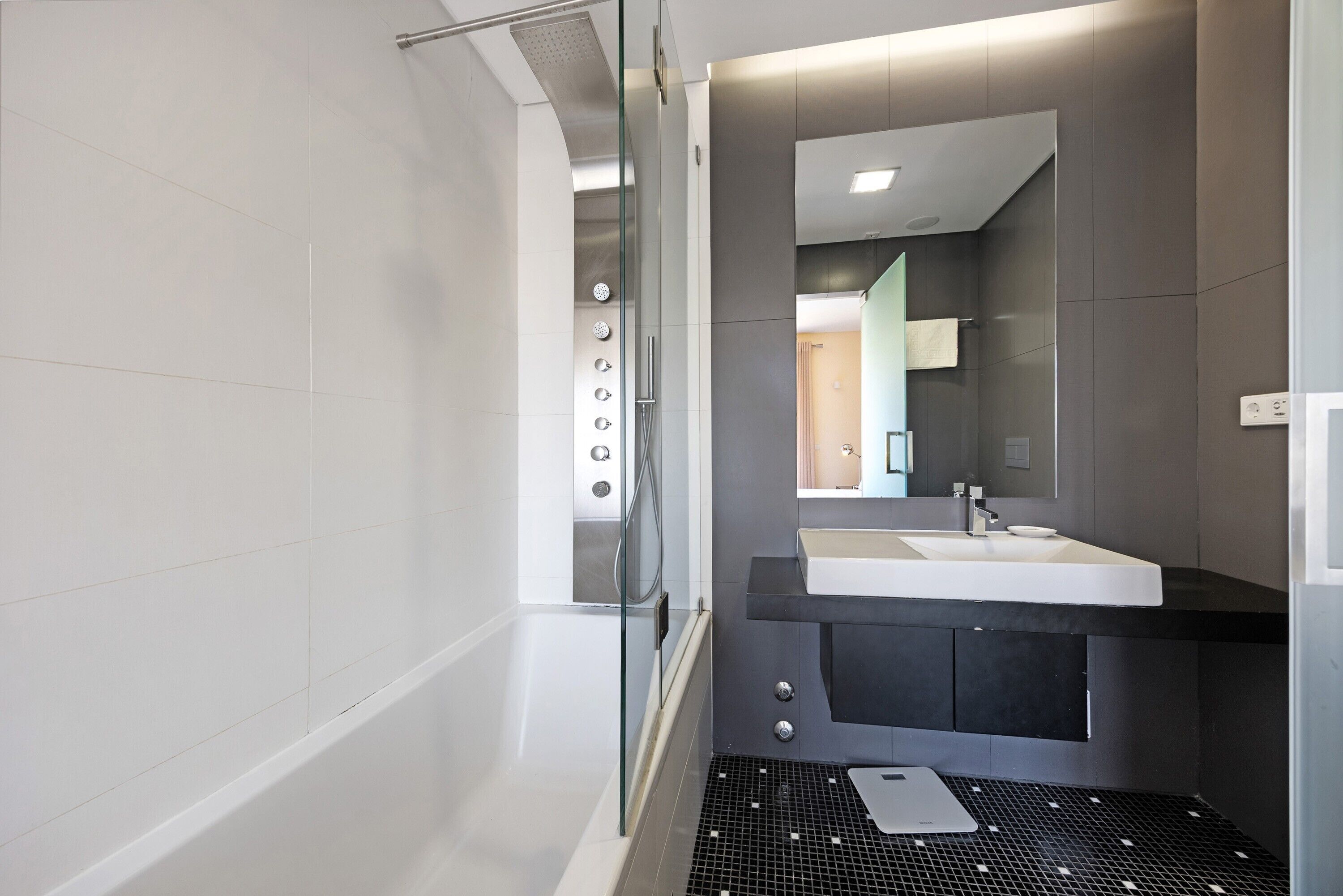 A modern bathroom with a glass shower enclosure, a white sink, and a large mirror.