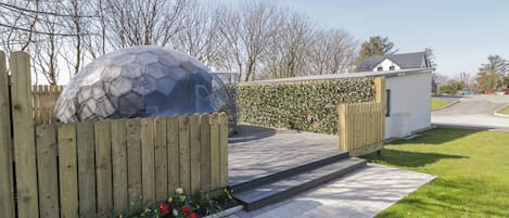 A modern building with a glass dome structure, a wooden fence, and a paved pathway leading to a small white building.