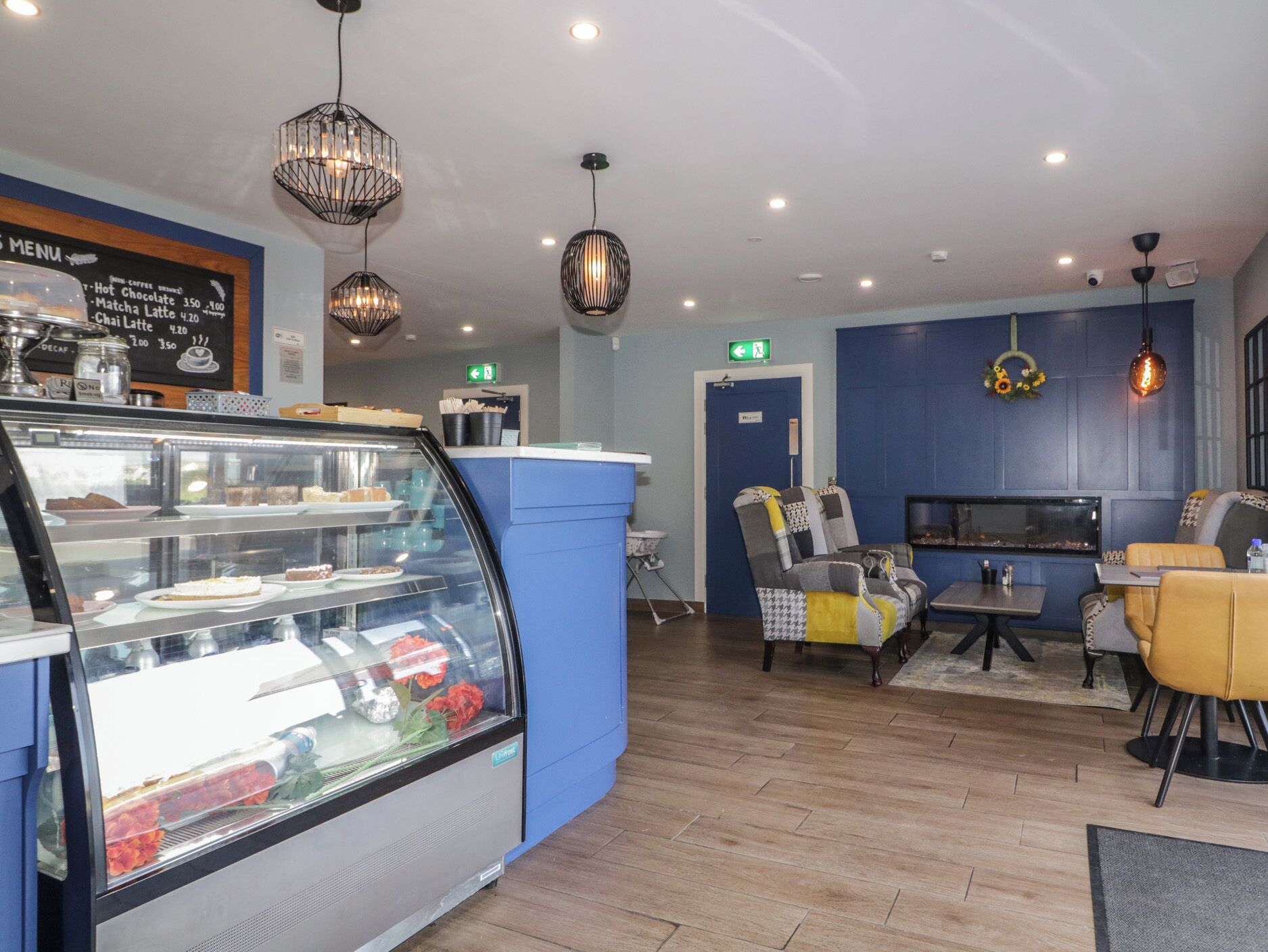 A modern cafe with a glass display case, blue walls, and contemporary furniture.