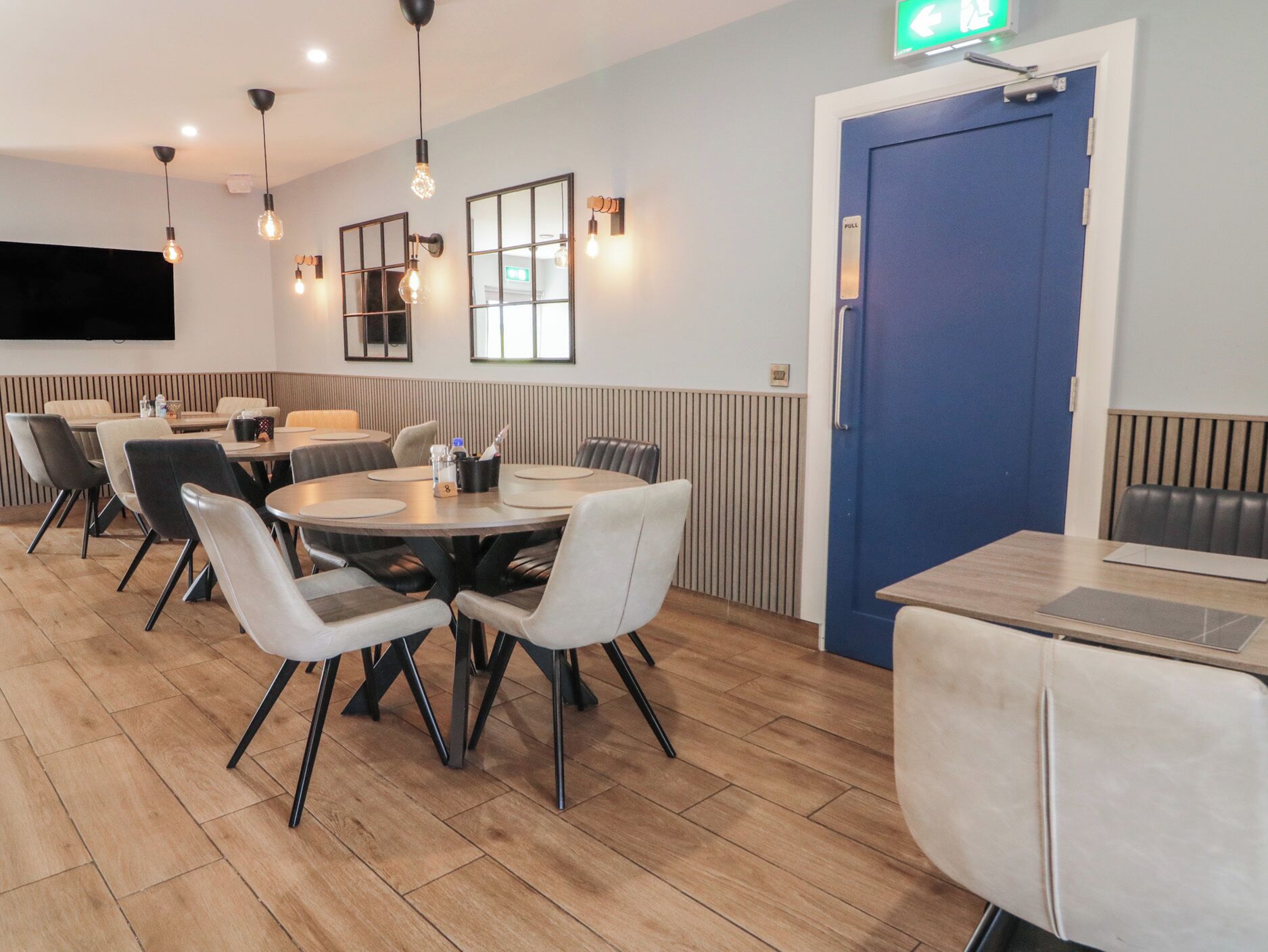 A modern dining area with round tables and chairs, a blue door, and pendant lighting.